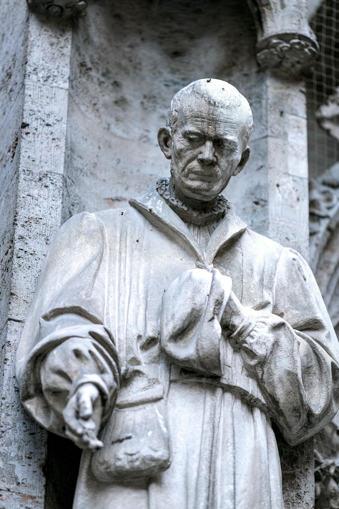 photo of a statue of a European philosopher or wise priest outside of a church, his hand is extending down signifying his willingness to help