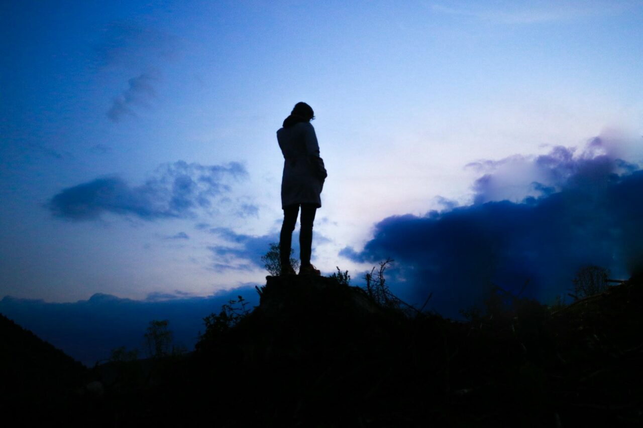 photo of a single person standing silhouetted against the rapidly darkening blueish sky